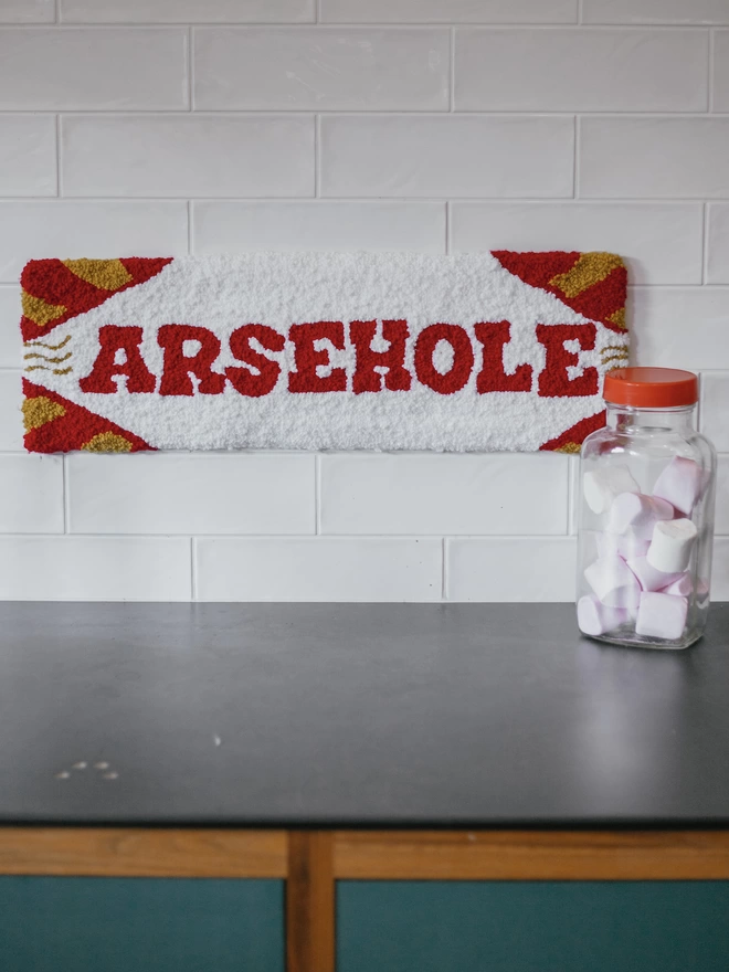 'Arsehold' Handmade Tufted Rug/Wall Hanging seen in a kitchen with a tub of marshmallows.