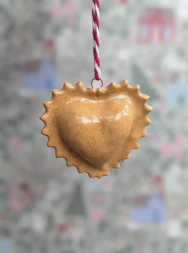ceramic heart ravioli christmas decoration. a small ceramic ravioli decoration hanging from red and white thread.