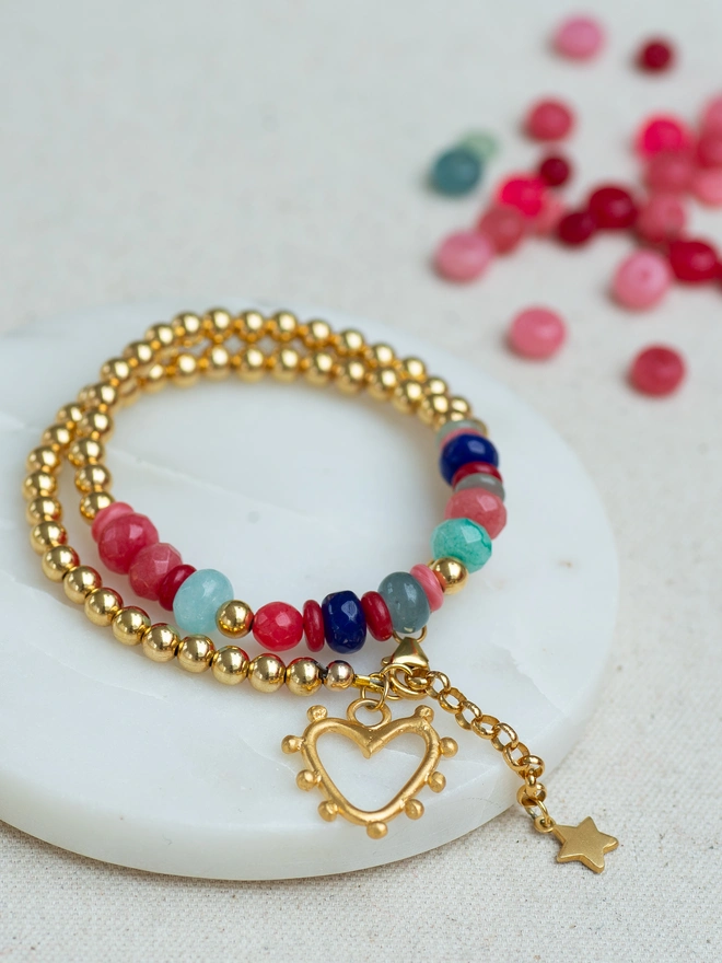 The Love Drunk Wrap Bracelet blends sleek metal beads with vibrant jade for a bold pop of colour and shine. Finished with a mini studded heart and delicate star charm, this double wrap bracelet is made for stacking or wearing solo. A joyful charm bracelet designed to celebrate confidence, colour and everyday sparkle.