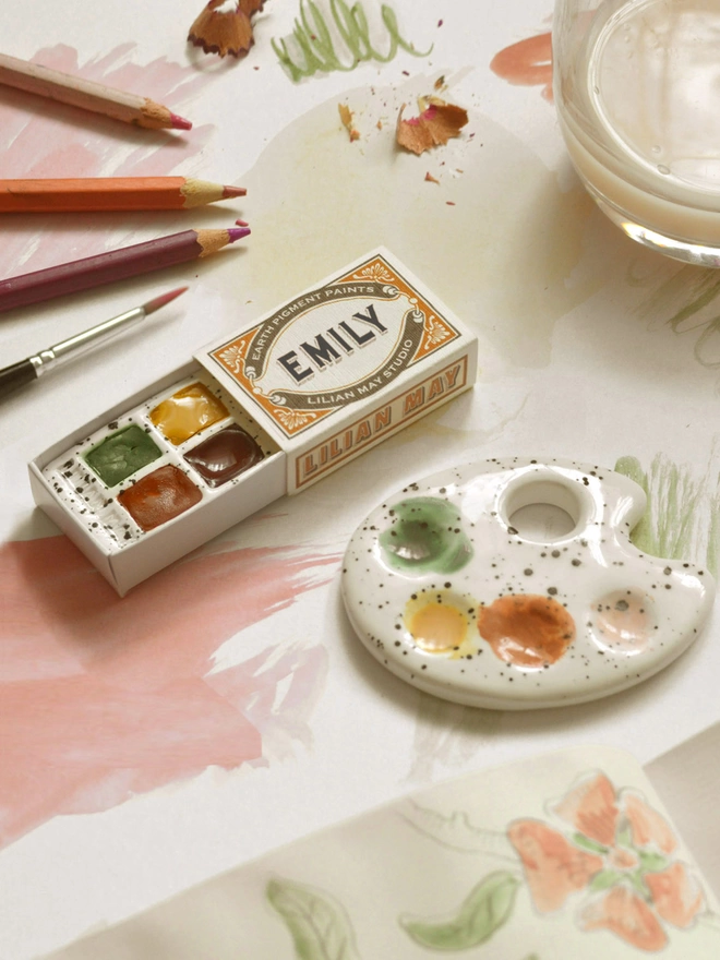 Personalised watercolour earth pigment set and mini palette on a desk with sketchbook and brush.