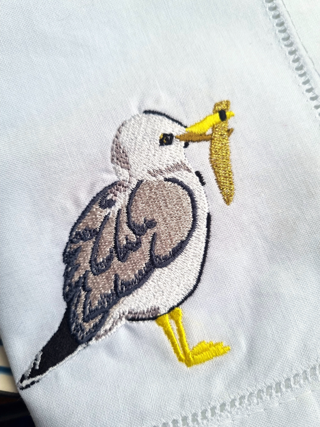 a seagull with a golden chip embroidered onto a white napkin