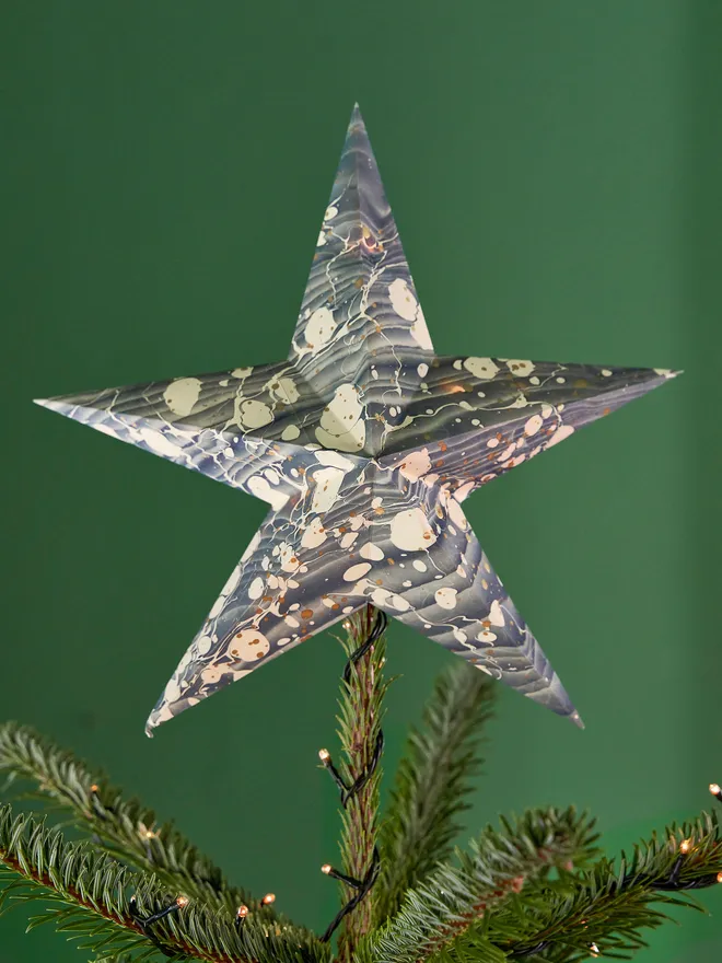 Blue and grey toned marbled paper star tree topper, on top of a Christmas tree against a green background