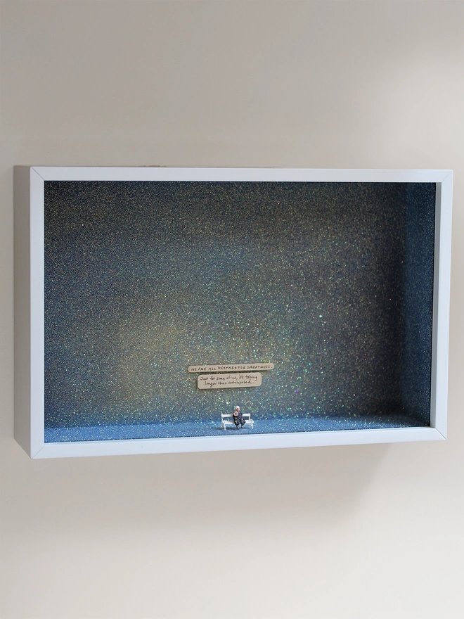 Miniature scene in an artbox showing a tiny old lady sitting on a bench, set against a sparkling purple-blue-grey backdrop (full artwork). 