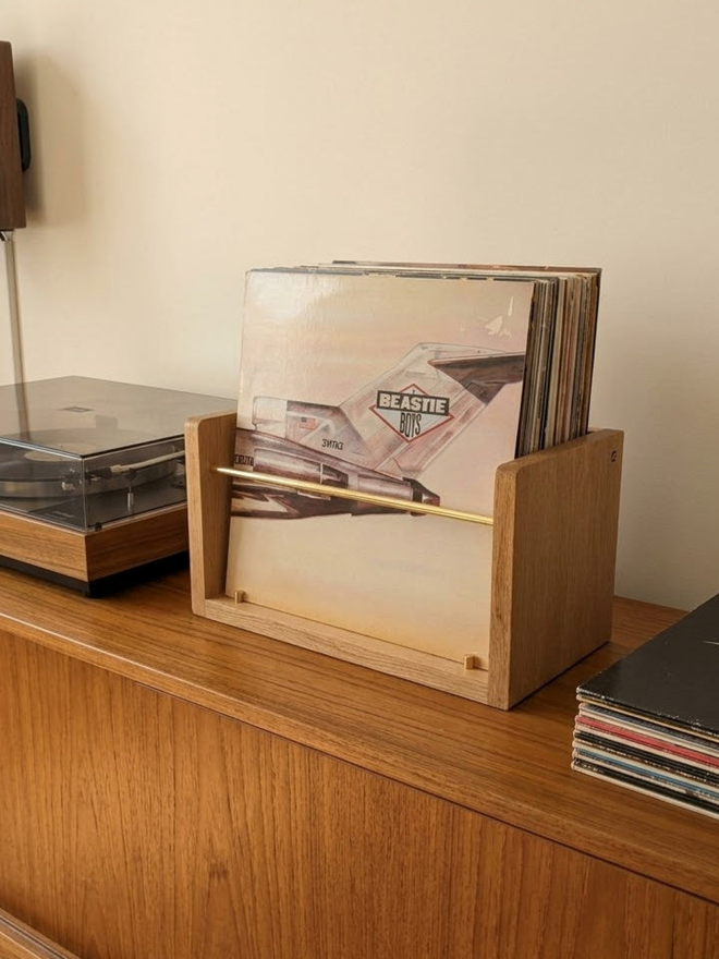 Compound LP Browser Slim in solid oak holding vinyl records on a wooden sideboard beside a turntable