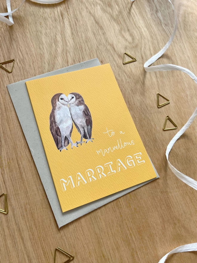 a greetings card with a bright yellow background featuring two kissing barn owls and the phrase ‘to a marvellous MARRIAGE”