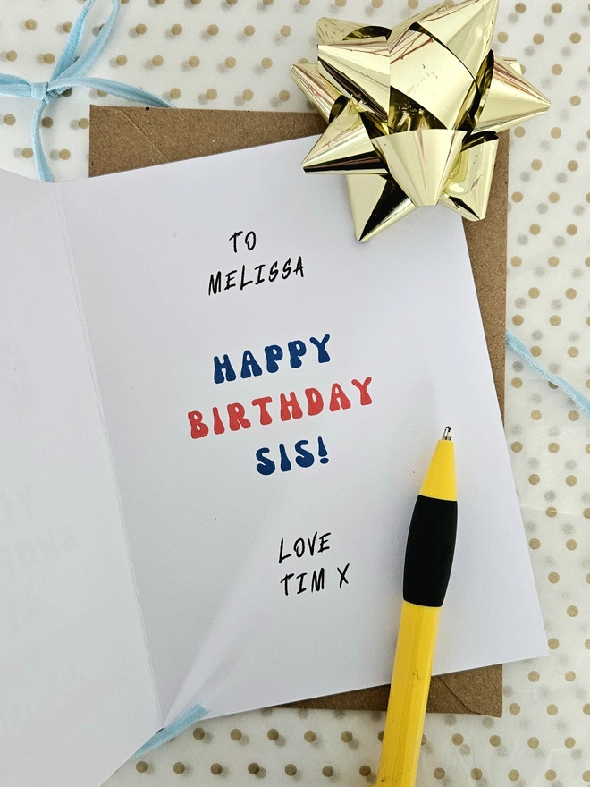 A photograph of the inside of a card that shows you how to personalise it, it says To Melissa Happy Birthday Sis Love Tim Kiss in colourful letters with a retro typeface