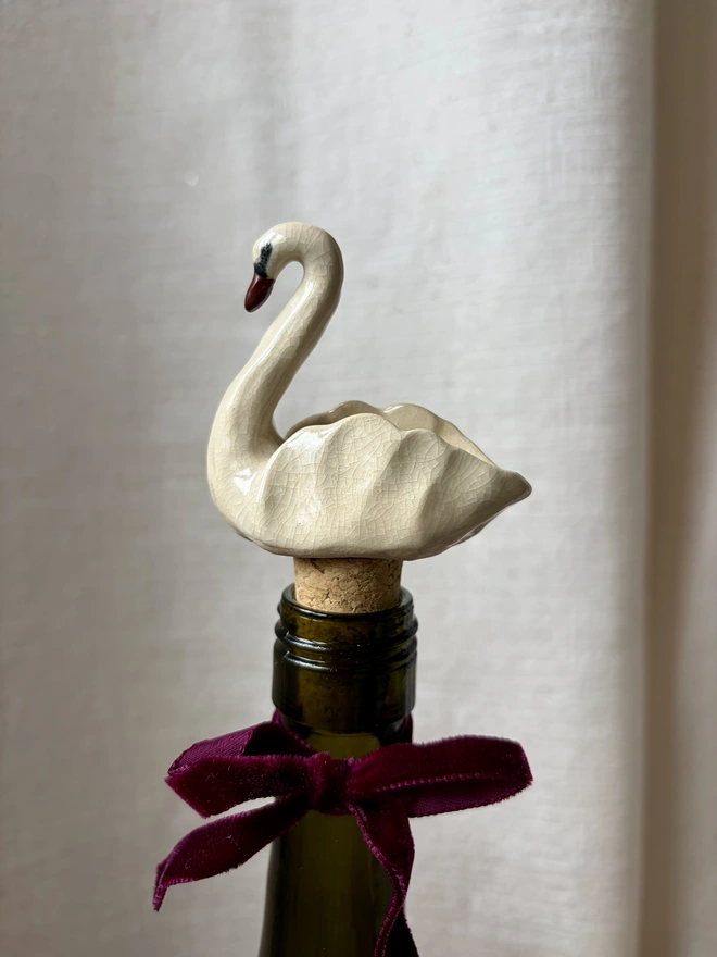 A white crackle ceramic, swan shaped bottle stopper, in a bottle of wine