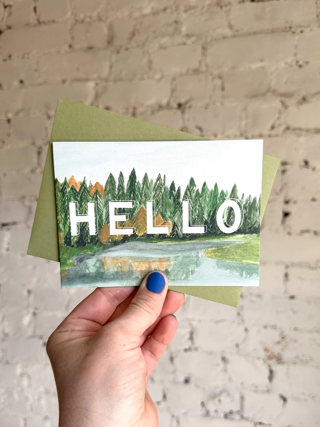 a greetings card featuring an illustration of some of the Taiga landscape with the text “hello” with a green envelope