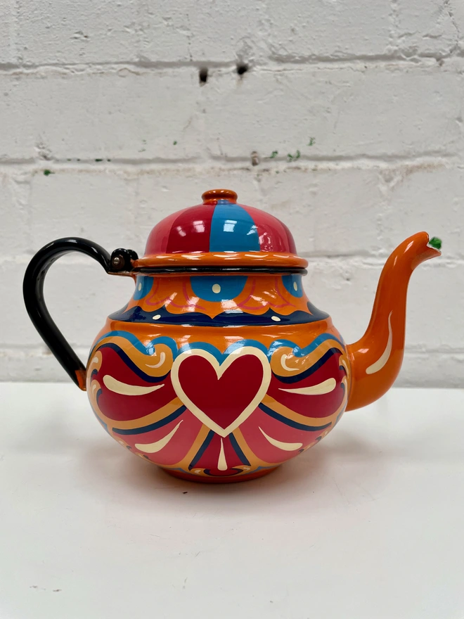 Orange vintage teapot with hinged lid, hand painted with a traditional fairground inspired design in pink, red, yellow and blue.