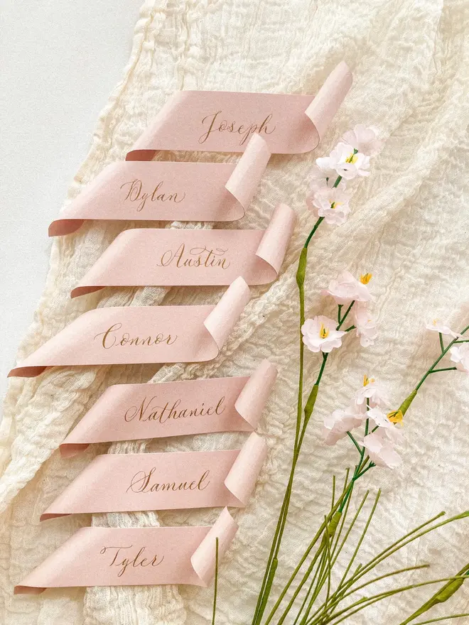 blush pink scroll calligraphy wedding place cards. pink scrolls on muslin background.