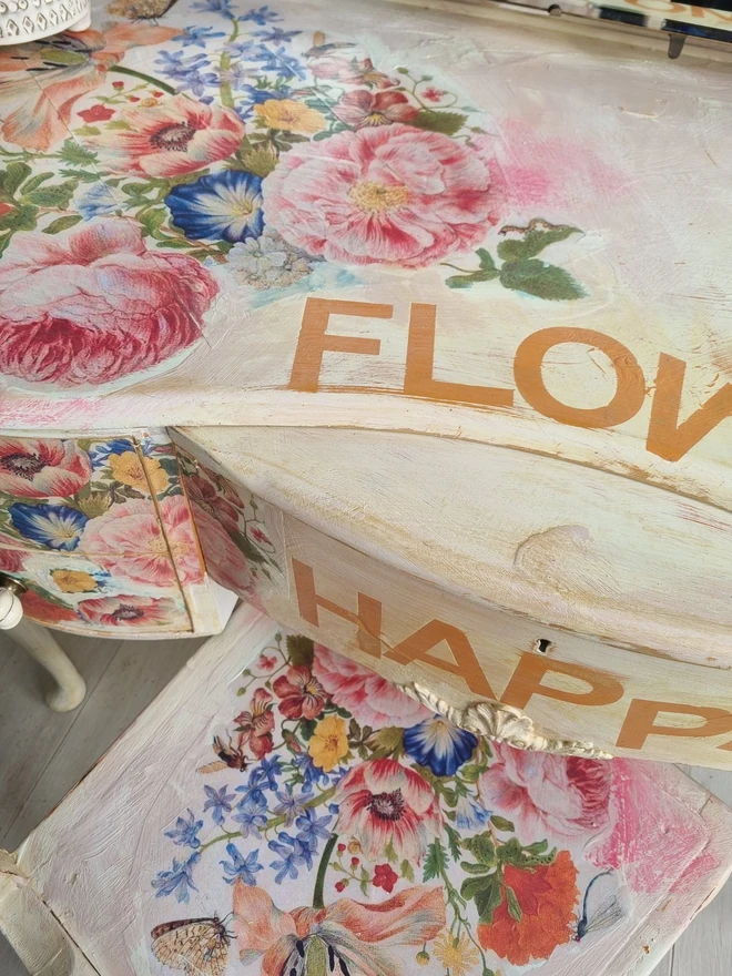 An antique kidney-shaped dressing table with chair and a trio of mirrors. Upcycled in cream and pale pink with decoupage florals in oranges and pinks. Text across the table read ‘flowers make me happy’ in the orange of the undercoat.