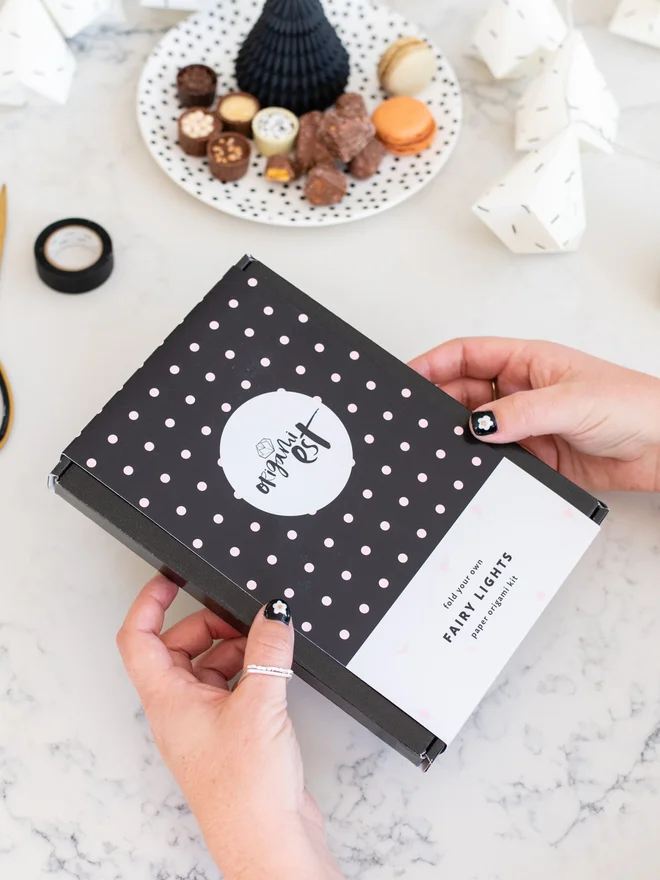Woman's hands holding origami fairy lights kit with snacks and premade fairy lights in the background