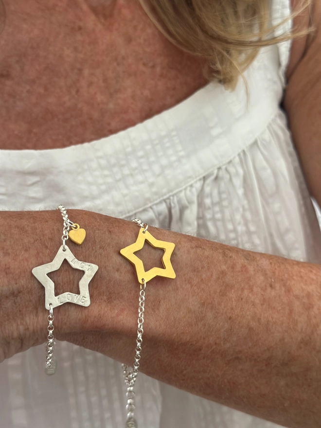model wears personalised sterling silver open star charm on a silver belcher chain bracelet with additional tiny heart charm in gold, and a version of the bracelet in gold