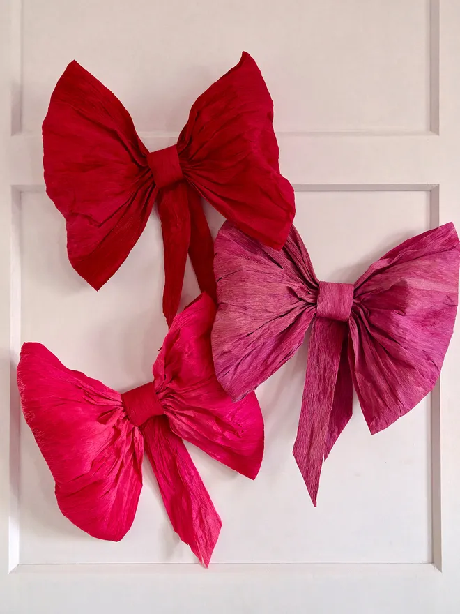 Large crepe paper pink and red bows. Three large paper bows hung on a white door