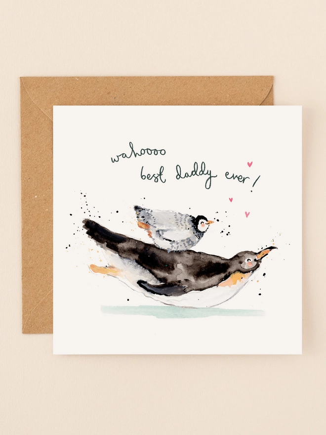 A charming illustration of a father penguin carrying a young penguin on its back, both joyfully surrounded by scattered hearts. The playful handwritten message "Wahoo Best Daddy Ever!" adds a heartwarming touch.