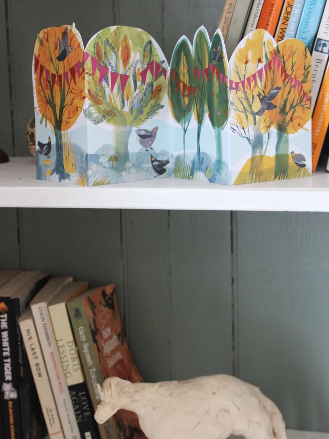 Happy Forest folded concertina card on a shelf above books and a horse sculpture