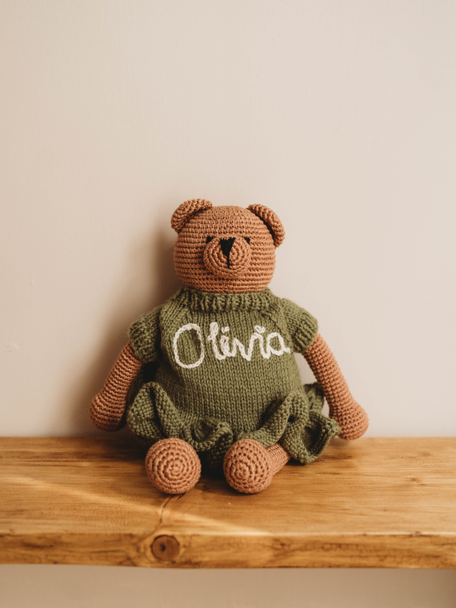 hand crochet brown teddy bear on wooden shelf wearing olive green hand knit dress