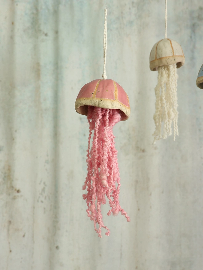 fuchsia pink hanging jellyfish decoration hangs in the forground with a white ceramic jellyfish hanging in the distance