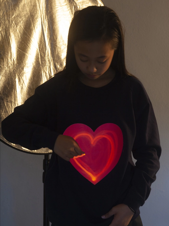 Girl with small penlight drawing a heart shaped image onto a glow in the dark heart sweat