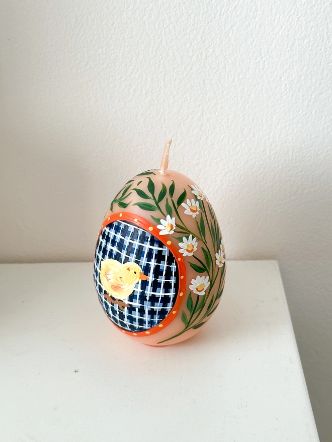 Hand Painted Easter Egg Candle Chick, an Easter egg candle sitting on a plain surface. It's Easter and floral design wraps around the egg. 