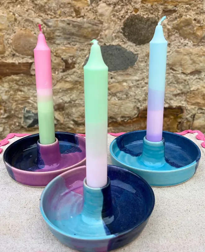 Landscape Candle Stick Holder, a collection of colourful candle stick holders accompanied by candles on a stone surface against a brick backdrop. 