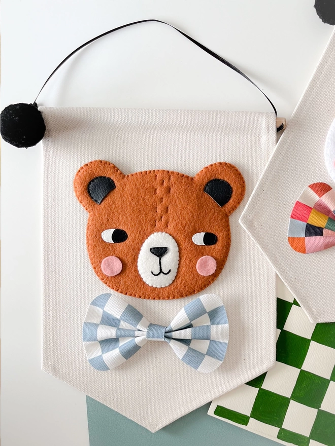 Brown bear banner on a cream background with a blue and white chequered bow tie