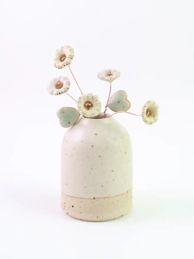 White and yellow pastel ceramic wildflowers with copper stems and two mint green heart leaves coming out of a speckled white ceramic vase