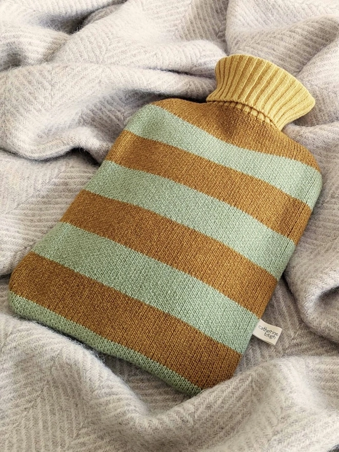 Lambswool Hot Water Bottle Cover, a colourful hot water bottle cover sitting on a blanket. 