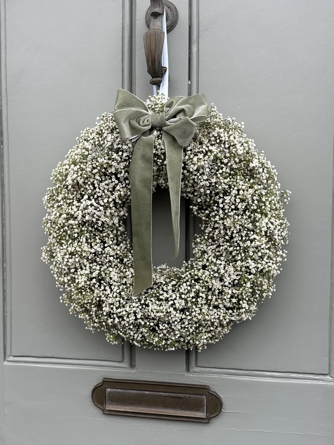 Fresh White Gypsophila Wreath with a Green Velvet Bow hanging on a grey door