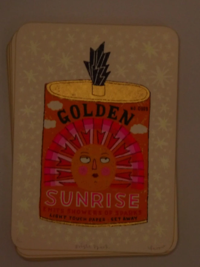 Bright Spark Sun Firework Screenprint, a colourful firework tin design on a white screenprint. The glow in the dark design is visible. 