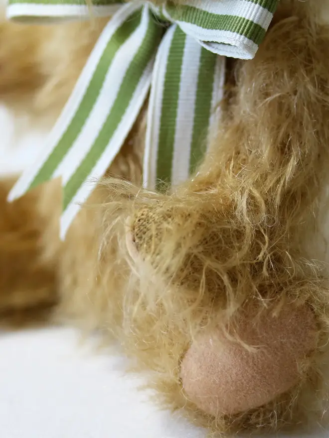 Handmade brown teddy bear sitting upright with a green striped ribbon bow against a plain background.