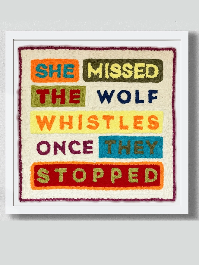 Typographic punch needle textile art "She missed the wolf whistles once they stopped" in bright wool type with coloured blocks mounted in white box frame