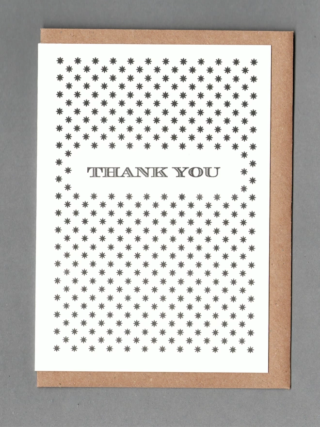 White card with black stars and black text reading 'Thank You' with a kraft envelope behind it