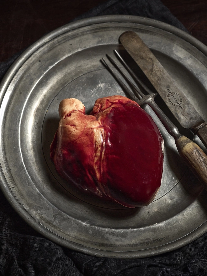 Realistic chocolate human heart on antique plate with knife and fork