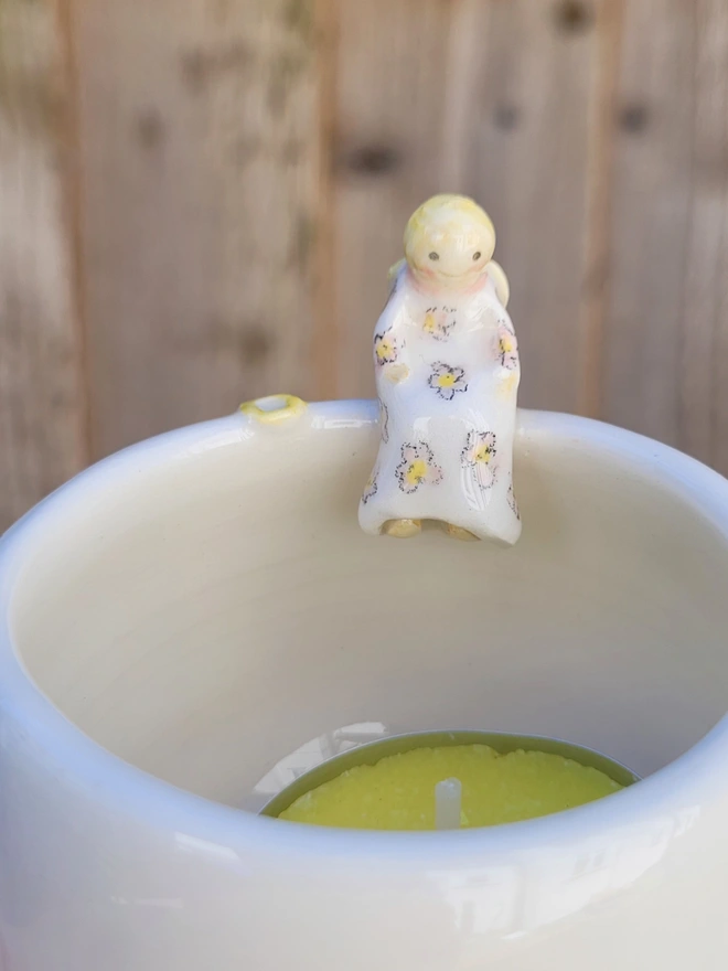 angel tealight with an angel sculpture sitting on the side of the white pottery pot 