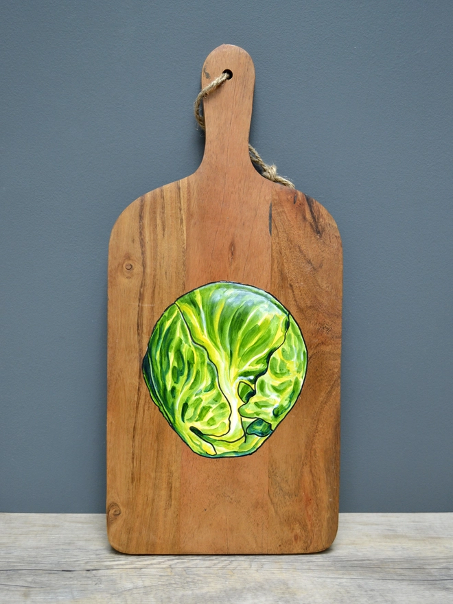 A wooden serving board with a handpainted design of Brussels sprouts