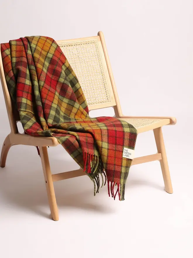 Buchanan Autumn Tartan Blanket, an orange blanket draped over a wooden chair on a white surface against a plain backdrop. 