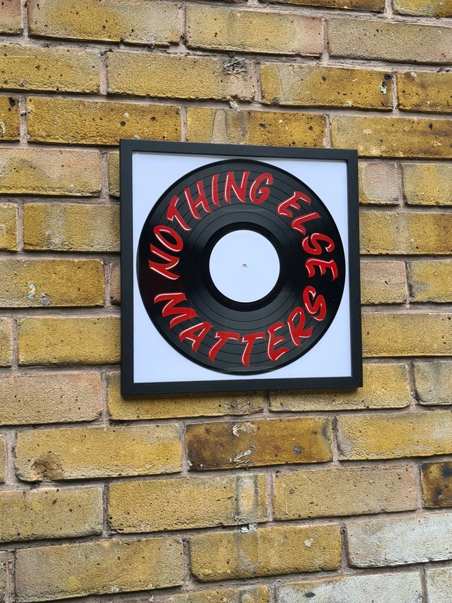 'Nothing Else Matters' Vinyl Artwork, a person holding a colourful vinyl artwork above a stone surface in frame on brick wall