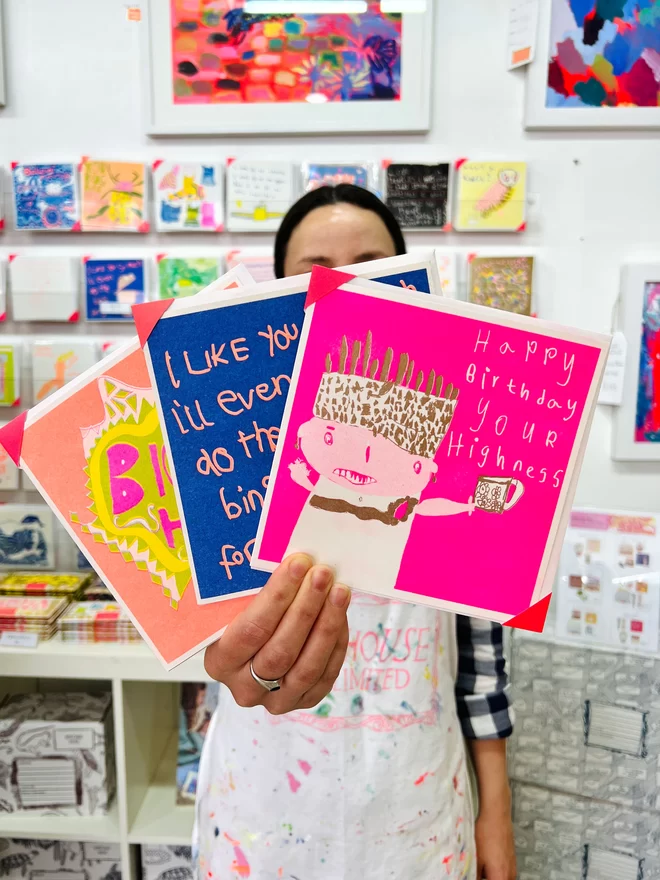 Artist holding a pink with flashes of gold riso printed birthday card that says Happy Birthday Your Highness