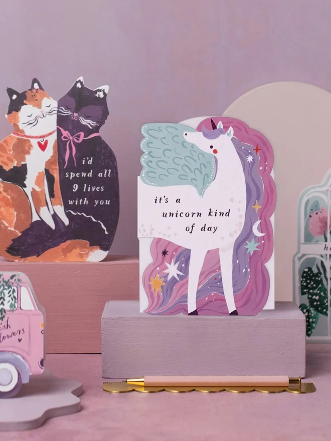 Unicorn Birthday Card standing on a pink plinth beside other illustrated greeting cards