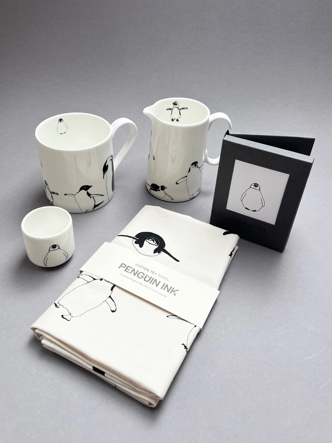 Collection of penguin decorated mugs, jugs and tea towel.