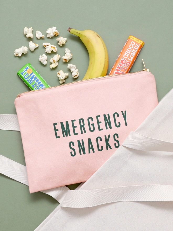 Emergency snacks pink zip pouch laying on a green background with snacks spilling out 