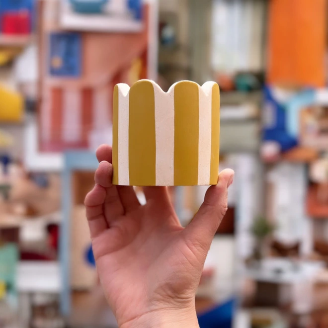 Yellow striped peachy pink scalloped pot. Held up against a colourful backdrop.