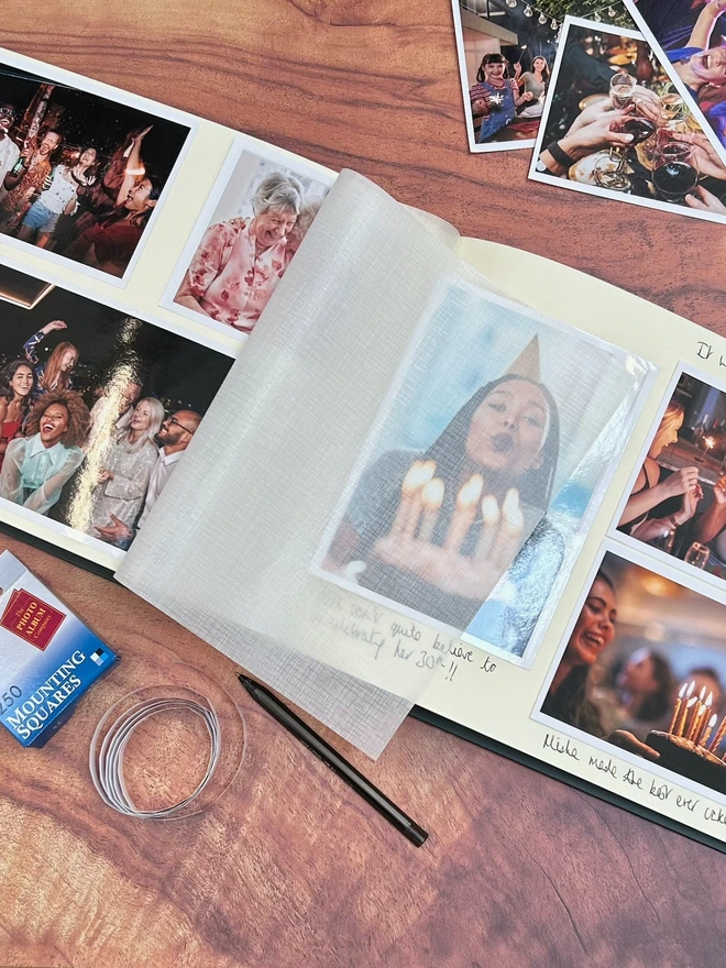 a landscape photo album is lying open on a wooden table and inside you can see lots of photos which have been stuck in. All the photos are of people having fun at parties