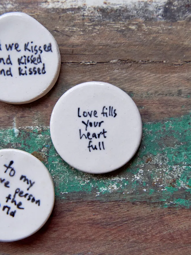 Small ceramic love token. Ceramic love tokens with phrases written on them in black on a wooden surface