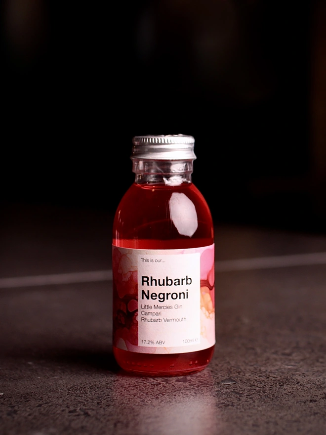 Mini Rhubarb Negroni bottle against a dark background