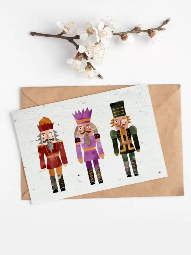 In the centre of the image is a card with three illustrated nutcrackers, above the card is a white flower sprig.