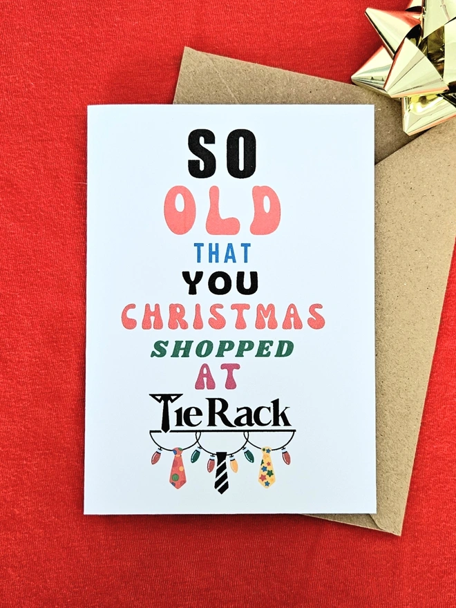 A photograph of the front of a humorous A6 greeting card illustrated using brightly coloured text and the retro shop logo. The text says so old you Christmas shopped at Tie Rack with illustrated loop fairy lights.