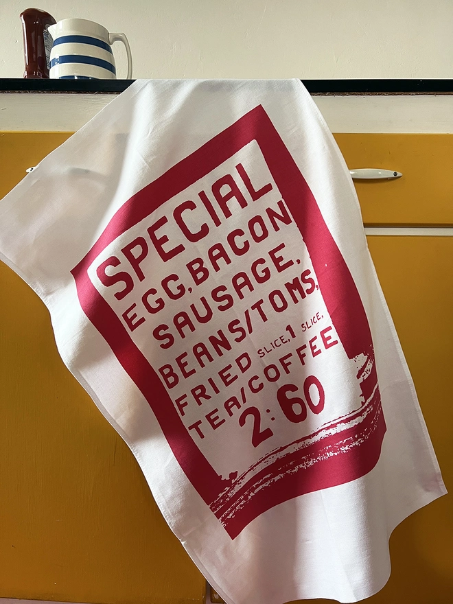Mr.PS Big Breakfast menu screenprinted tea towel hanging on a yellow cabinet