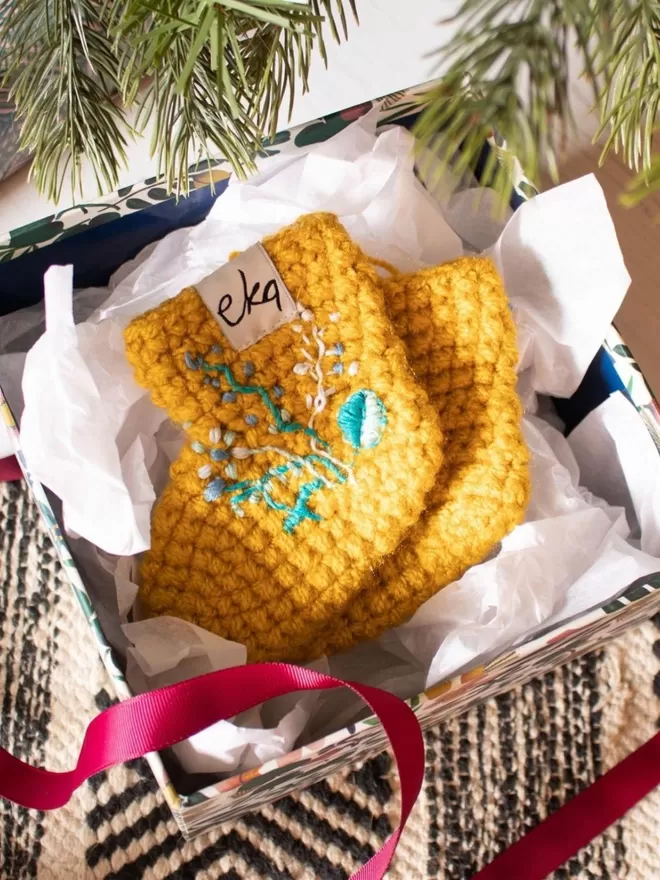 EKA crotched yellow boots with embroidered flowers seen in a box with ribbons.